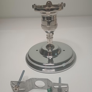 May include: A chrome-finished light fixture with a circular base and a bulb socket. A metal mounting bracket with screws is positioned below the fixture. The fixture is designed for overhead lighting.