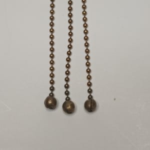 May include: Three gold-coloured chains with round metal beads and a bell at the end of each chain.