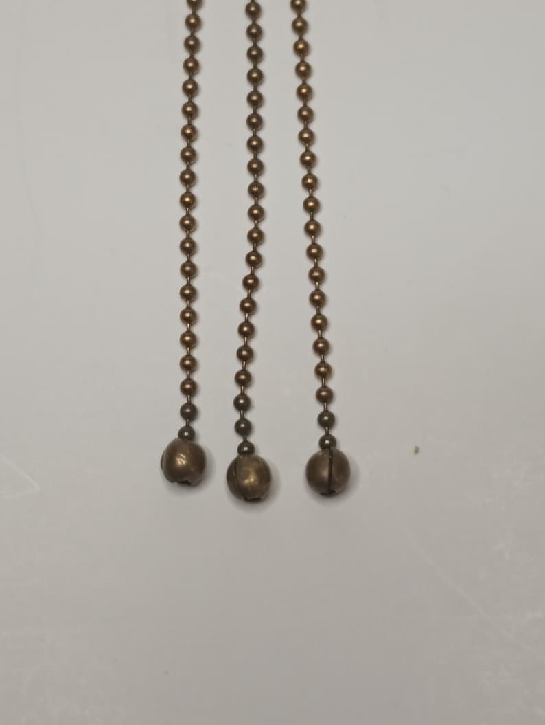May include: Three gold-coloured chains with round metal beads and a bell at the end of each chain.