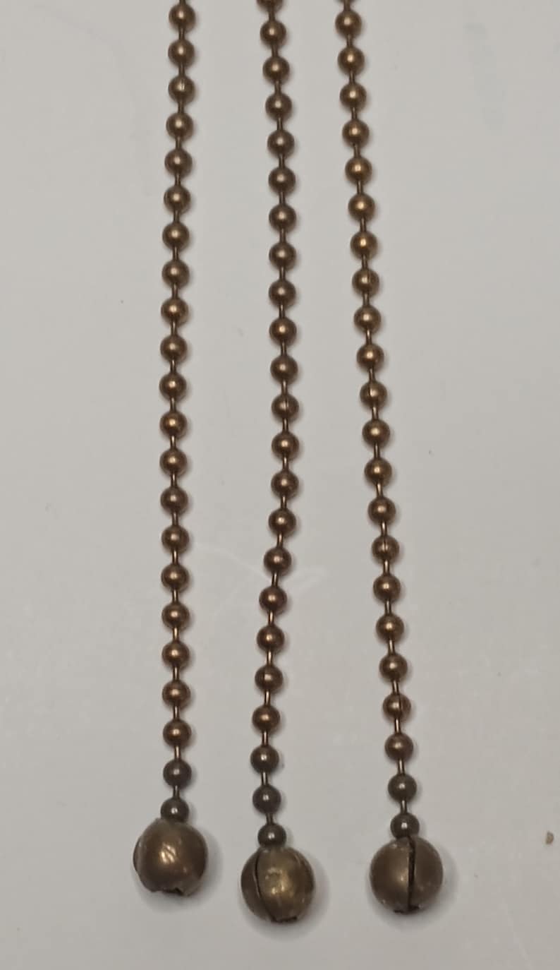 May include: Three gold-toned ball chains with a bell at the end of each chain.