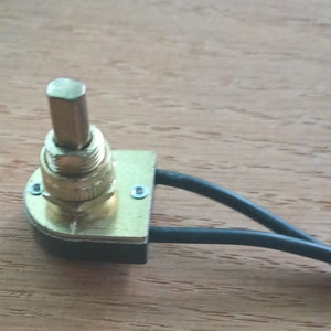 May include: A gold-colored rotary switch with a black base and two black wires attached. The switch has a small, round knob on top.