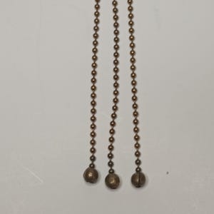 May include: Three gold-coloured chains with round beads and a ball at the end of each chain.