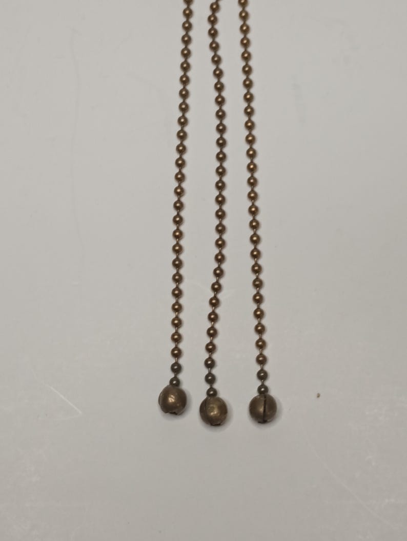 May include: Three gold-coloured chains with round beads and a ball at the end of each chain.
