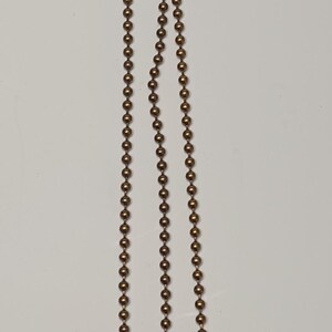 May include: Three gold-toned chains with round beads and a bell at the end of each chain.