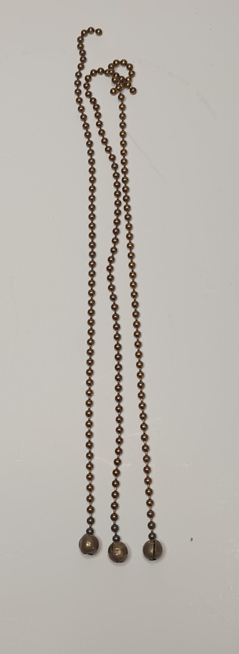 May include: Three gold-toned chains with round beads and a bell at the end of each chain.