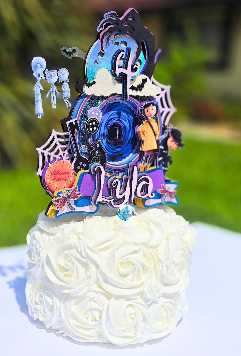 May include: A white cake with buttercream frosting, topped with a colorful, layered cake topper. The topper features characters and elements from a fantasy movie, including a girl in a yellow coat, a black cat, and the name "Lyla".
