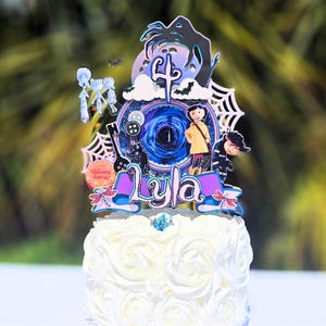 May include: A white cake decorated with white frosting roses, topped with a colorful cake topper. The topper features a character theme with the name "Lyla" and the number "4". The cake is set against a blurred green background.