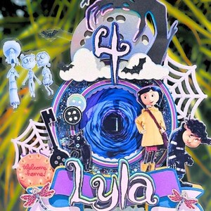 May include: A layered cake topper featuring characters and elements from the movie Coraline. The design includes the name "Lyla", a number "4", a black cat, a key, and a spiderweb. The color scheme includes blue, purple, and pink.