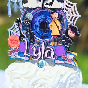 May include: A cake topper featuring characters and elements from the movie "Coraline." The topper includes a central portal design, the name "Lyla," and various character cutouts, all set atop a white frosted cake.