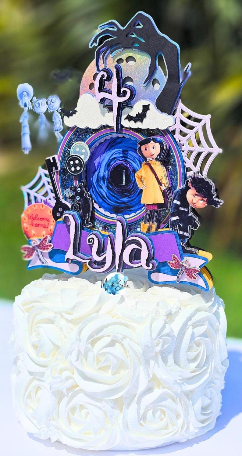 May include: A cake topper featuring characters and elements from the movie "Coraline." The topper includes a central portal design, the name "Lyla," and various character cutouts, all set atop a white frosted cake.