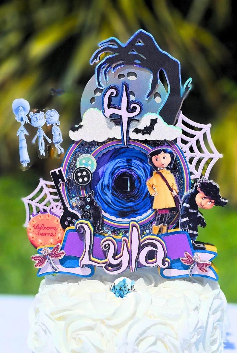 May include: A cake topper featuring characters and elements from the movie "Coraline." The design includes a central portal, the name "Lyla," and various character cutouts, all set against a backdrop of a white cake.