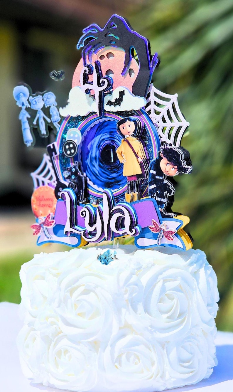 May include: A white cake with a decorative topper featuring characters and elements from the movie "Coraline." The topper includes the name "Lyla," a swirling portal, and other themed details. The cake is decorated with white frosting in a rose pattern.