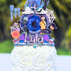 May include: A white frosted cake with a decorative topper featuring characters and elements from the movie "Coraline". The topper includes the name "Lyla", the number "4", and other themed decorations. The cake is decorated with white frosting roses.