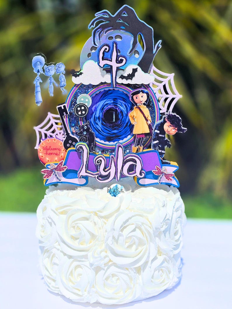 May include: A white frosted cake with a decorative topper featuring characters and elements from the movie "Coraline". The topper includes the name "Lyla", the number "4", and other themed decorations. The cake is decorated with white frosting roses.