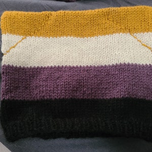 May include: A knitted scarf with four horizontal stripes in yellow, white, purple, and black. The scarf is made with a simple knit stitch.