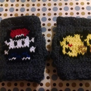 May include: Two knitted gray fingerless gloves with embroidered pixel art designs. One glove features a red, white, and blue pixelated character, while the other glove features a yellow pixelated character.