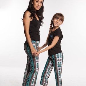 May include: Two people wearing black shirts and matching teal, brown, and white patterned pants. The woman is holding the girl's hand.