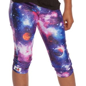 May include: Purple, blue, and pink galaxy print leggings with a red and orange planet design. The leggings are cropped and have a cuffed hem.