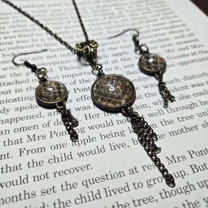May include: A necklace and earrings set with a bronze chain and a pendant featuring a round, clear glass cabochon with a brown and white pattern. The earrings have a similar design with dangling chains.