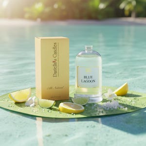 Puede incluir: Una botella de vidrio transparente y una caja dorada con el texto "Daniella's Candles Collection" y "Blue Lagoon" se exhiben sobre una hoja verde. Rodajas de lim&oacute;n y lima, flores blancas y sal rodean la botella.