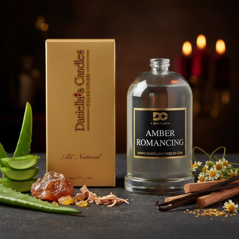 May include: A gold box and a clear glass bottle with a black label that reads "Amber Romancing" are displayed. The box says "Daniella's Candles Collection" and "All Natural". The bottle contains a liquid and is surrounded by botanicals.