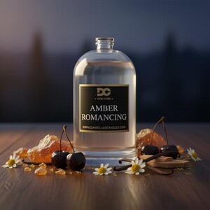 May include: A clear glass bottle with a black and gold label that reads "AMBER ROMANCING" sits on a wooden surface. The bottle is surrounded by cherries, vanilla beans, and small white flowers. The website www.daniellascandles.com is also visible.