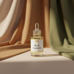 Puede incluir: Botella de vidrio transparente con cuentagotas, llena de l&iacute;quido amarillo. La etiqueta dice "Blue Lagoon". El fondo presenta tela drapeada en tonos beige y verde.