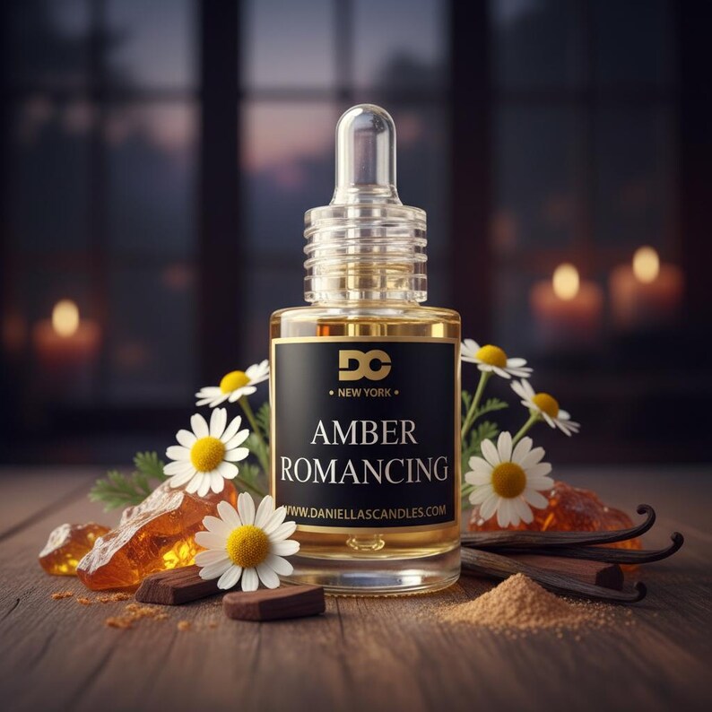 May include: A clear glass bottle with a dropper, labeled "Amber Romancing" with the website address. The bottle is surrounded by white daisies, amber-colored crystals, and vanilla beans. The background is a blurred view of a window and candles.
