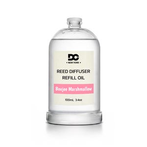 May include: A clear glass bottle containing reed diffuser refill oil. The label features the text DC NEW YORK, REED DIFFUSER REFILL OIL, and Boujee Marshmallow in a pink bar, with a volume of 100mL 3.4oz printed at the bottom of the label.