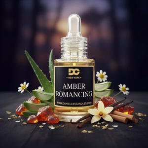 May include: A clear glass bottle with a dropper, filled with amber-colored liquid. The label reads "Amber Romancing" with the text "DC New York". The bottle is surrounded by aloe vera, flowers, amber stones, vanilla beans, and cinnamon sticks.