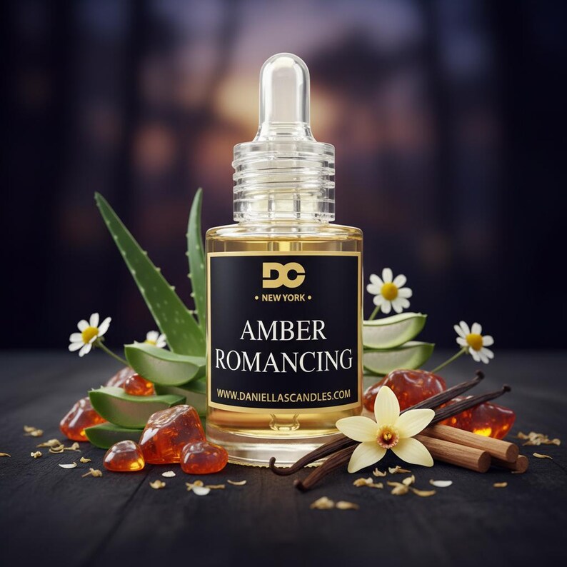 May include: A clear glass bottle with a dropper, filled with amber-colored liquid. The label reads "Amber Romancing" with the text "DC New York". The bottle is surrounded by aloe vera, flowers, amber stones, vanilla beans, and cinnamon sticks.