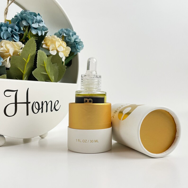 May include: A white and gold cosmetic bottle with a dropper, next to a matching cylindrical container. The bottle is labeled "1 FL OZ / 30 ML". The background includes a white floral arrangement and the word "Home".
