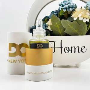 May include: A white and gold essential oil bottle with a clear dropper, black label with gold logo, and a gold base. A white cylinder with a gold logo and the words "NEW YORK" is to the left. The website address is printed on the base.