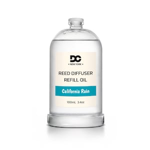 May include: A clear glass bottle containing reed diffuser refill oil. The label features the text DC NEW YORK, REED DIFFUSER REFILL OIL, California Rain, and 100mL 3.4oz. The bottle has a simple cylindrical shape with a small screw-top cap.