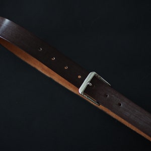 May include: A brown leather belt with a silver buckle. The belt has multiple holes for adjusting the size.