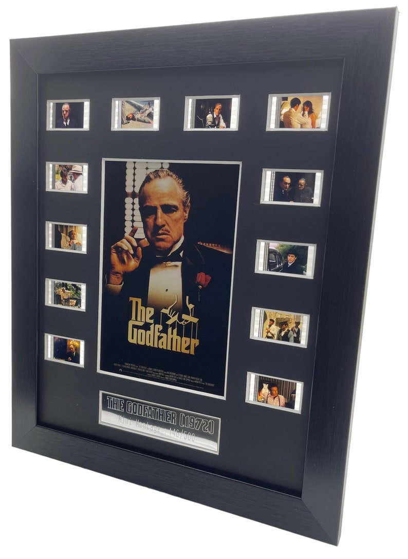 Puede incluir: Un p&oacute;ster de pel&iacute;cula enmarcado de El Padrino con un marco negro y una placa plateada que dice "The Godfather 1972, Film Montage 146/500". El p&oacute;ster presenta un primer plano de Marlon Brando como Don Vito Corleone. Hay 10 tiras de celdas de pel&iacute;cula alrededor del p&oacute;ster.