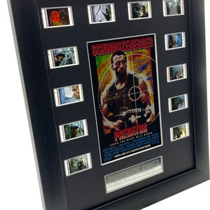 Puede incluir: Una colección enmarcada de carteles de películas y celdas de película con Arnold Schwarzenegger en la película "Depredador" de 1987. El cartel presenta un primer plano de Schwarzenegger sosteniendo un arma con el texto "Schwarzenegger" y "Depredador" en él. Las celdas de película están dispuestas en una cuadrícula alrededor del cartel.