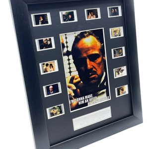 May include: A black framed movie cell display featuring a close-up of Marlon Brando as Don Vito Corleone from the film The Godfather. The display includes 9 film cells from the movie and the quote "I'm gonna make him an offer he can't refuse."