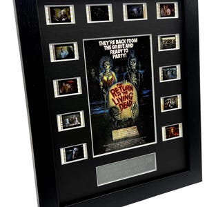 Könnte beinhalten: Gerahmtes Filmbild mit Filmzellen und einem Filmposter von "The Return of the Living Dead". Das Poster zeigt Zombie-Charaktere und den Text "They're back from the grave and ready to party!" Der schwarze Rahmen hat eine silberne Plakette.