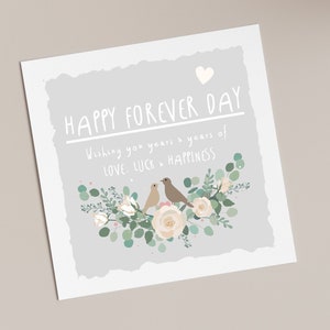 May include: A grey card with the text "Happy Forever Day" and "Wishing you years & years of love, luck & happiness". Two brown birds are perched on a white rose with green leaves and white flowers.