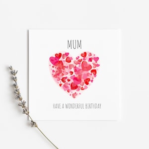 May include: A white card with the word "MUM" in black text. A large pink heart made of smaller pink and red hearts is in the center of the card. The text "HAVE A WONDERFUL BIRTHDAY" is below the heart.