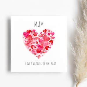 May include: A white card with the word "MUM" in black text. A large pink heart made of smaller pink and red hearts is in the center of the card. The text "HAVE A WONDERFUL BIRTHDAY" is below the heart.