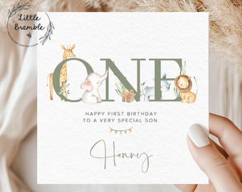 May include: A square birthday greeting card featuring the word ONE in large sage green letters. A watercolor giraffe, elephant, gift, rhino, and lion are integrated into the letters. Text reads HAPPY FIRST BIRTHDAY TO A VERY SPECIAL SON Henry.