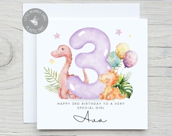 May include: A birthday card with a watercolor illustration of a pink dinosaur, a large purple number 3, and two other dinosaurs. The card reads "Happy 3rd Birthday to a Very Special Girl" and "Personalise Me".