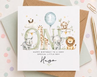 May include: A square birthday greeting card featuring the word ONE in large green letters decorated with watercolor illustrations of a rhino, giraffe, elephant, lion, and monkey. A blue balloon with the number 1 floats above. Text reads: HAPPY BIRTHDAY TO A VERY SPECIAL LITTLE BOY Hugo.