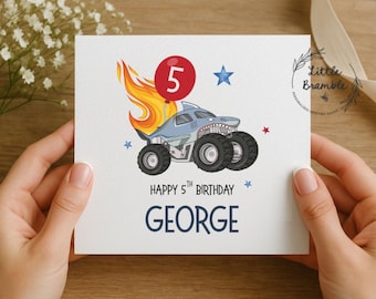 May include: A white birthday card featuring a shark-themed monster truck with a red balloon displaying the number 5. The card includes the text "Happy 5th Birthday GEORGE" in navy blue.