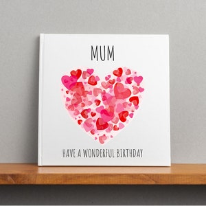May include: A white card with the word "MUM" in black text and a large pink and red heart made of smaller hearts. The text "HAVE A WONDERFUL BIRTHDAY" is below the heart.