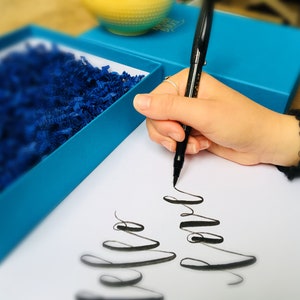 May include: A person's hand writing with a black pen on a white piece of paper. The writing is in cursive and says "Happy" and "Love".