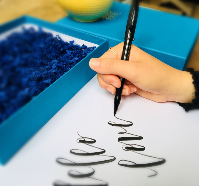 May include: A person's hand writing with a black pen on a white piece of paper. The writing is in cursive and says "Happy" and "Love".