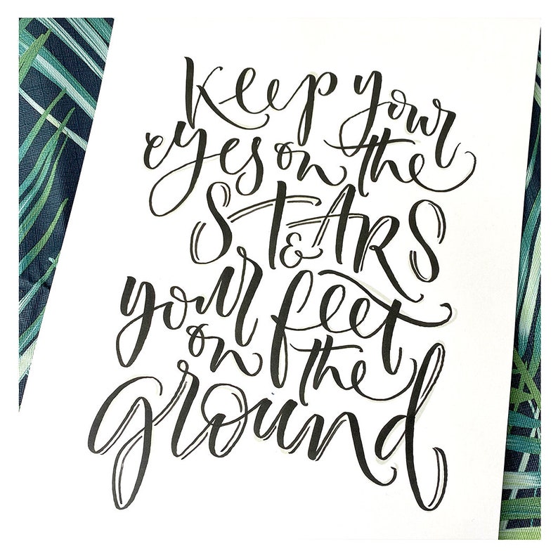 May include: Black and white calligraphy art print with the quote "Keep your eyes on the stars and your feet on the ground".